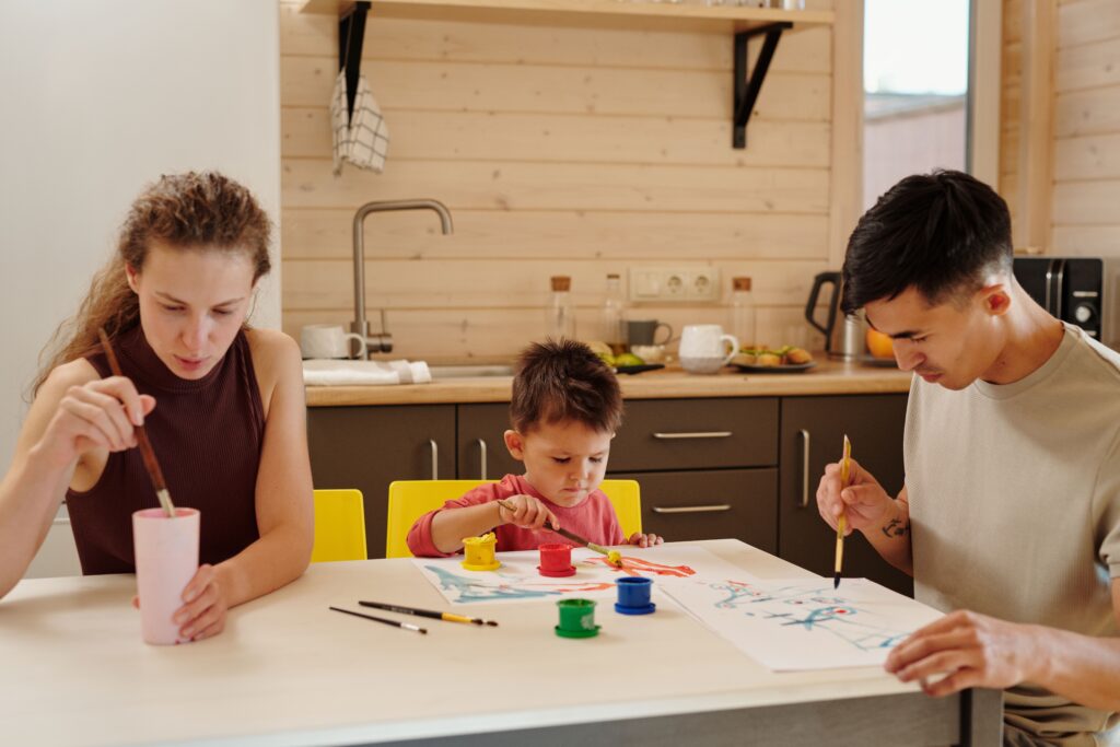A family enjoying creative painting time together in a cozy kitchen setting.